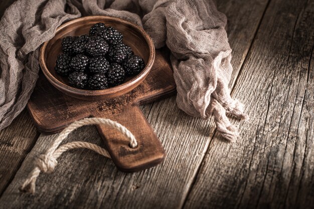 Blackberries in plate on wood background.