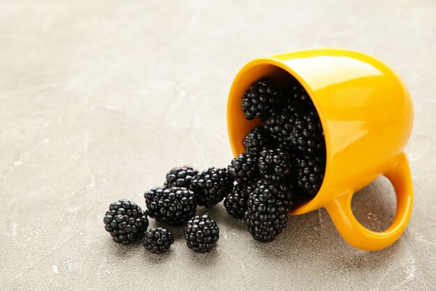 Blackberries in yellow cup on a grey concrete table