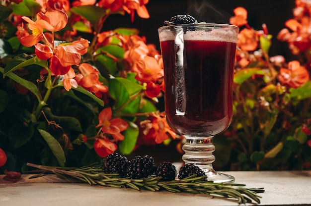 Blackberry mulled wine with rosemary in a glass cup on flowers background