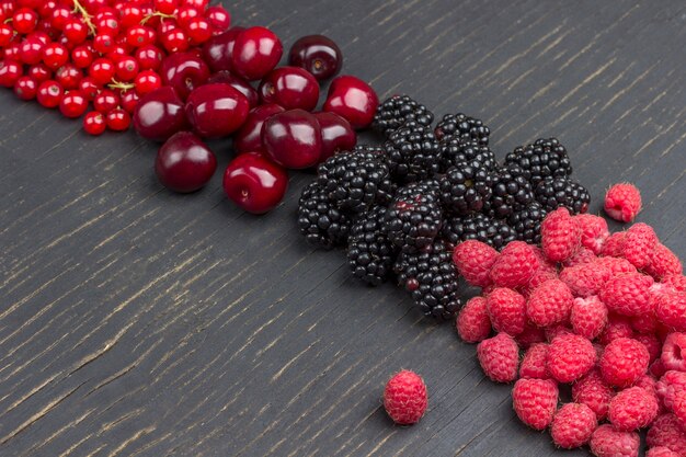 Blackberry, red currants, cherry, and raspberry on Black surface. Copy space. Flat lay