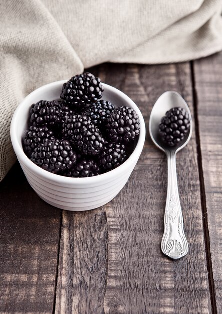 Blackberry in white bowl and spoon on grunge wooden board.