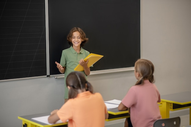 At the blackboard. A boy in green tshirt standing at the blackboard