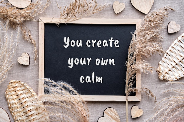 Blackboard caption You create your own calm on chalk board Monochromatic flat lay with natural pampas grass dry reeds wood hearts on beige textile linen tablecloth