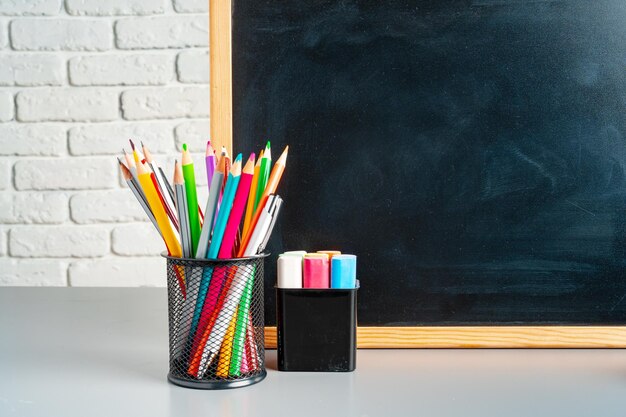 Blackboard and cup of colorful pencils and chalk on desk