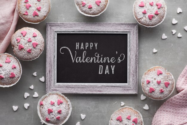 Blackboard framed with sugar-sprinkled muffins with pink and white fondant icing hearts, text