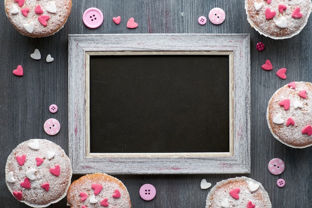 Blackboard framed with sugar-sprinkled muffins with pink and white fondant icing hearts