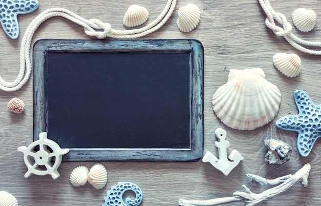 Blackboard  with frame made of sea shells, stones, rope and star fish on light wood