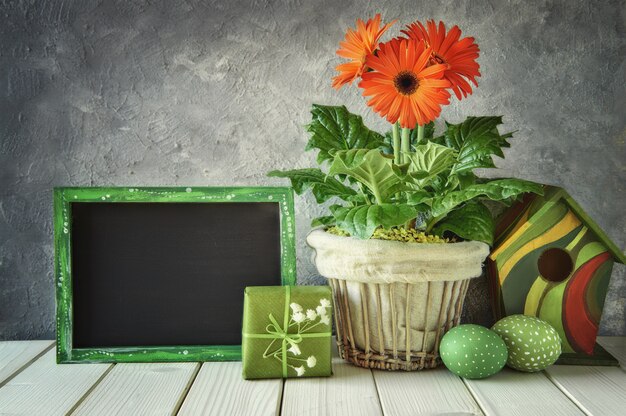 Blackboard with spring decorations: orange gerberas, lily of the valley, birdhouse and easter eggs,