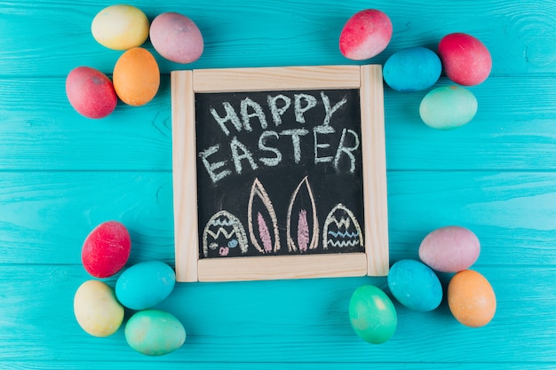 Blackboard with the text to Easter around eggs on a blue wooden background. 