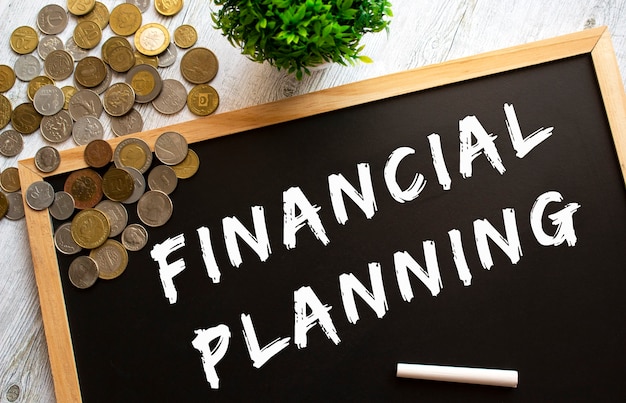 Blackboard with the text FINANCIAL PLANNING and metal coins on a gray wooden table. Financial concept.