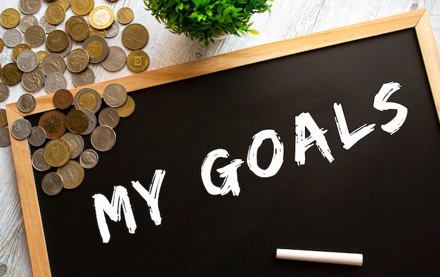 Blackboard with the text MY GOALS and metal coins on a gray wooden table.