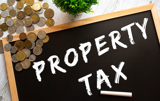 Blackboard with the text PROPERTY TAX and metal coins on a gray wooden table