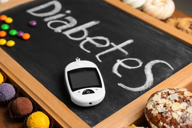 Blackboard with word Diabetes sweets and digital glucometer on table