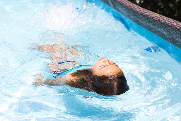 スイミング プールの黒髪の女の子が水の中でリラックスして横たわっているプール水泳水着子供夏リラックス休暇リゾートと旅行のコンセプト