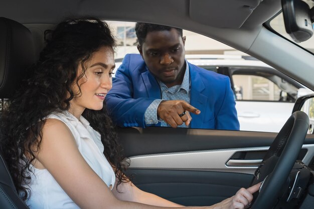 Blackhaired lady driver and dealer examine car in showroom