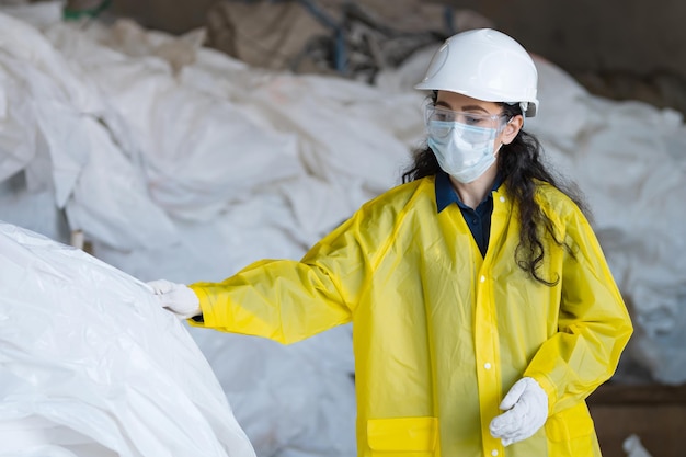 Blackhaired lady worker in mask and protecting glasses sorts trash in waste processing plant Supervisor prepares garbage for sorting in factory yard