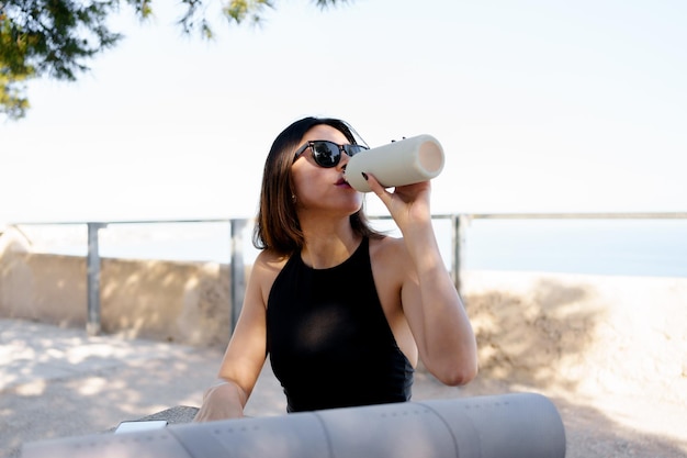 Blackhaired woman drinks water after her yoga exercises