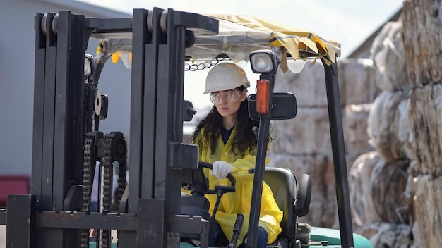 Photo blackhaired worker driving excavator for sorting trash at plant longhaired woman wearing hardhat controls process at waste sorting factory