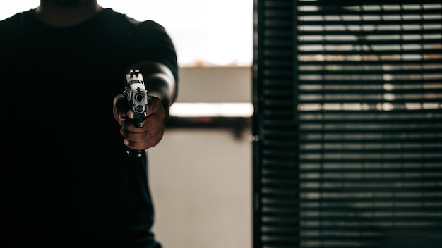 Преступник в черной рубашке с пистолетом врывается в дверь и направляет пистолет на преступную концепцию.