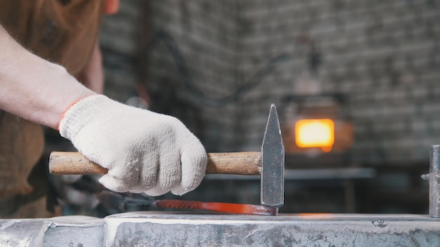 Blacksmith bends iron rod on the anvil with hammer, metal work, close up, telephoto