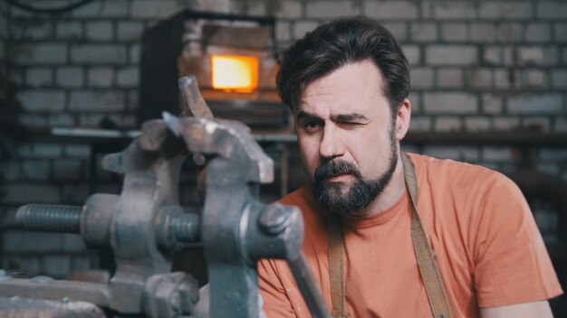 Blacksmith bends metal knife with gripe in workshop forge, portrait, telephoto