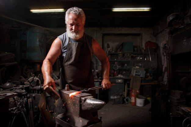 Blacksmith craftsman in apron works in blacksmith's shop