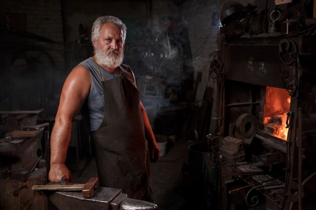 Photo blacksmith craftsman in apron works in blacksmith's shop