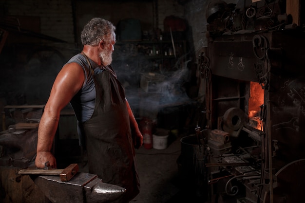 L'artigiano fabbro in grembiule lavora nella bottega del fabbro