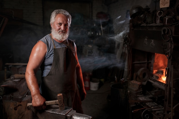 Blacksmith craftsman in apron works in blacksmith's shop