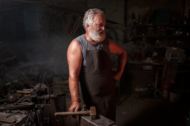 Blacksmith craftsman in apron works in blacksmith's shop