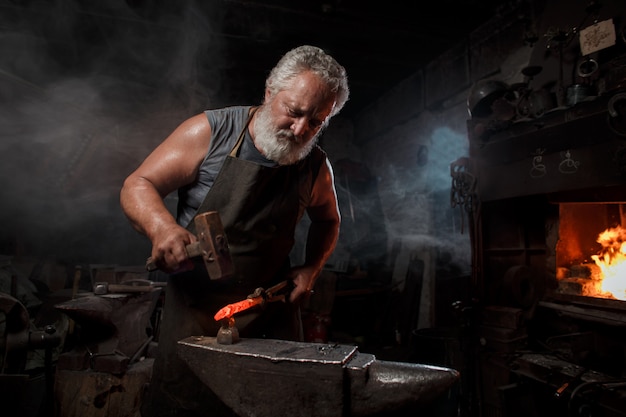 Blacksmith craftsman in apron works in blacksmith's shop