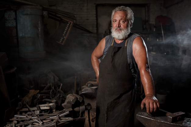 Blacksmith craftsman in apron works in blacksmith's shop