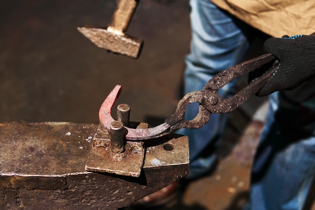 Photo blacksmith forges a horseshoe on the anvil with bending fork, close-up