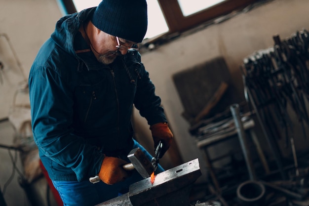 Blacksmith forges and makes metal detail with hammer and anvil at forge