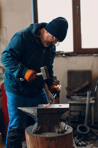 Photo blacksmith forges and makes metal detail with hammer and anvil at forge