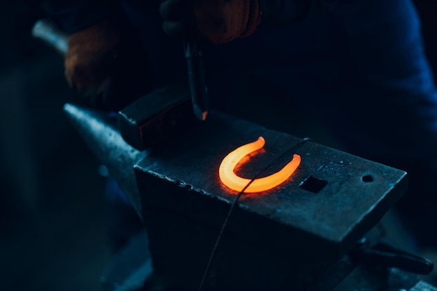 Blacksmith forges and makes metal detail with hammer and anvil at forge