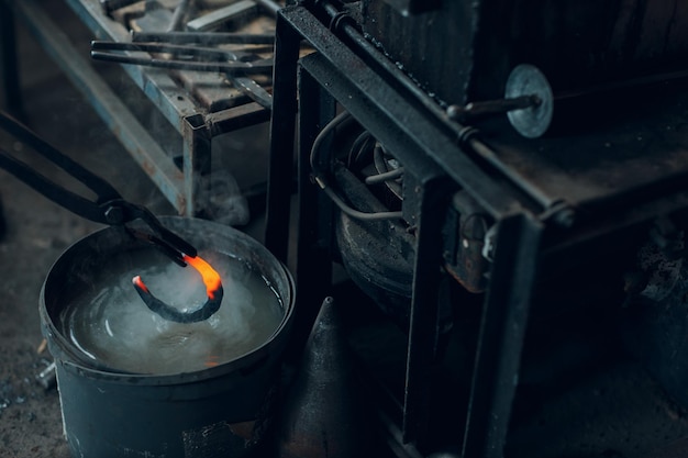 Blacksmith forges and tempering metal horseshoe in jar with water at forge