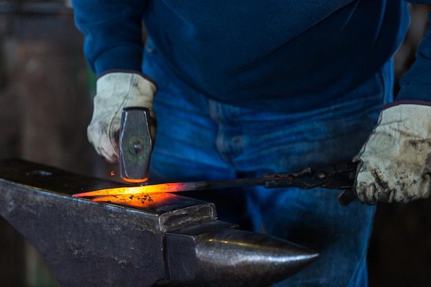 Foto un fabbro che forgia il ferro caldo sull'incudine.