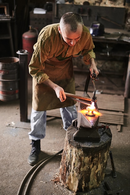 The blacksmith heats the gas burner the metal product on the anvil