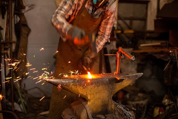 The blacksmith manually forging the molten metal on the anvil in smithy with spark fireworks Blacksmith's workshop