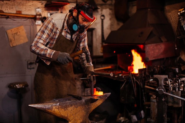 The blacksmith manually forging the molten metal on the anvil in smithy with spark fireworks Blacksmith's workshop