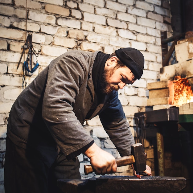 The blacksmith manually forging the red-hot metal on the anvil.