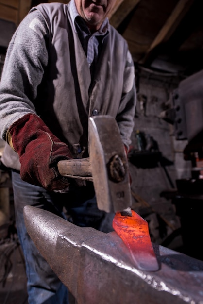 blacksmith manually forging the red hot molten metal on the anvil in traditional smithy workshop. Blacksmith working metal with hammer in the forge