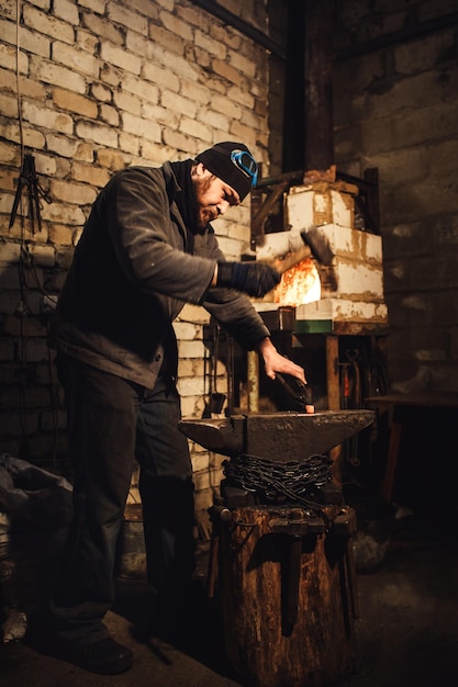 The blacksmith manually forging the redhot metal on the anvil