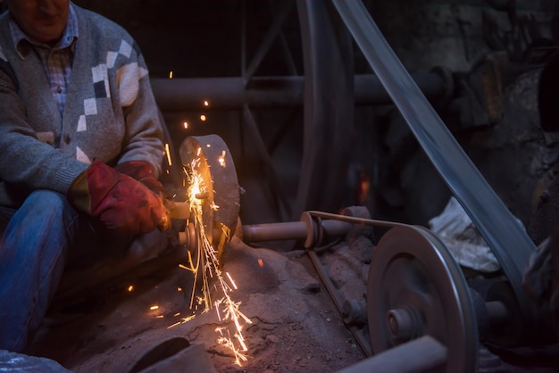 the blacksmith polishing metal products making sparks while using a grinding machine in his traditional workshop