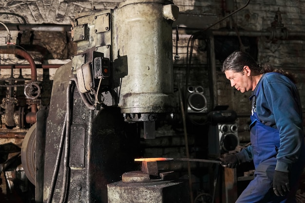 Blacksmith processes a hot workpiece with a pneumatic hammer in a workshop