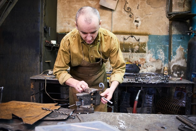 The blacksmith shapes the metal using a vise