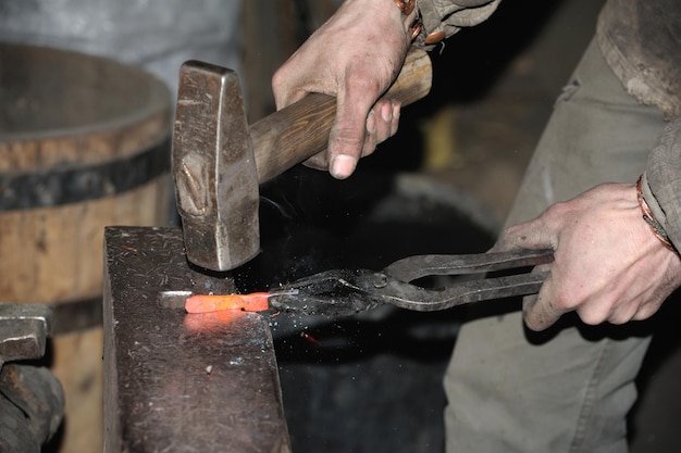 Blacksmith working metal with hammer on the anvil in the forge