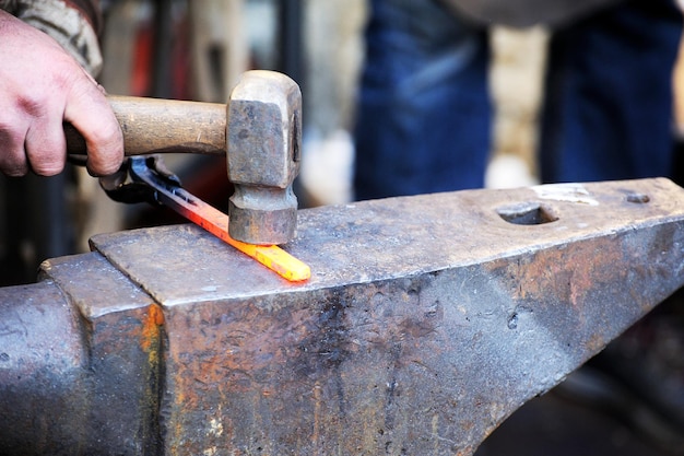 Blacksmith working metal with hammer on the anvil in the forge