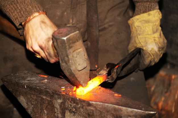 Blacksmith working metal with hammer on the anvil in the forge